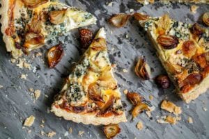 An onion and blue cheese tart cut into wedges with crispy onions scattered around it.