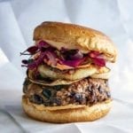 A black bean mushroom burger topped with onions, sauce, and purple leaves.