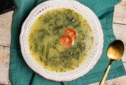 A white bowl of caldo verde, or Portuguese kale soup with thinly sliced kale and a single chorizo coin floating in the center.