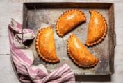 Four curried cauliflower and potato pasties in a metal baking dish with a pink and white striped towel on the edge.
