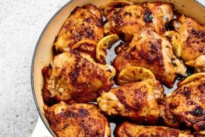 Nine roast lemon chicken thighs in a round Dutch oven with lemon slices tucked between them.