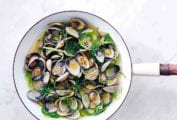 A white enamel wok filled with sake-steamed clams, broth, and scallions.