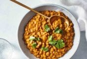 A white bowl filled with tikka masala lentil, garnished with cilantro, with a wooden spoon resting inside.