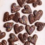 Heart shaped vegan gluten-free chocolate sugar cookies decorated with sprinkles.