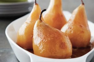 Four wine poached pears in a shallow white baking dish.