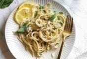 Two white plates topped with lemon basil pasta with lemon slices on the side and a gold fork resting on the side of each plate.