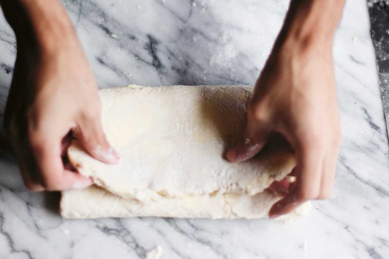 A person folding quick puff pastry on a marble counter.