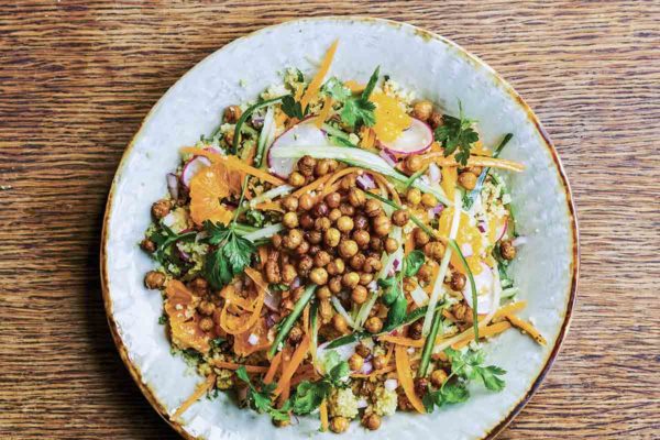 Roasted chickpea salad on a gold-rimmed plate, with orange segments, couscous, cilantro, and shaved carrot.