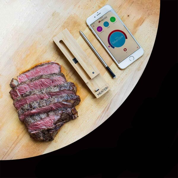 Wireless Meat Thermometer in the middle of smart phone and cut steak.