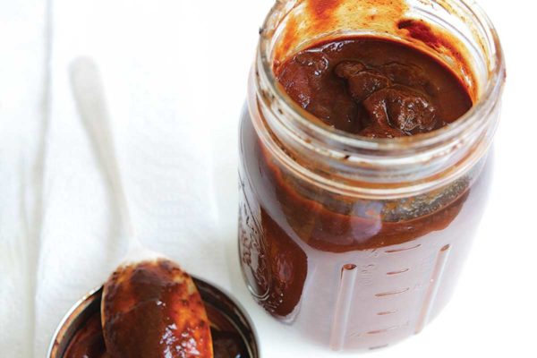 An open Mason jar of adobo sauce with a spoon resting on the lid beside it.