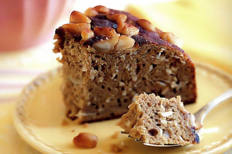 A slice of banana and macadamia nut coffee cake on a yellow plate with a fork holding a bite of it.
