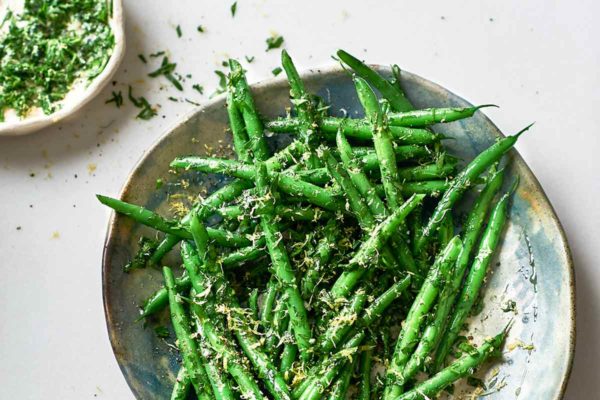 A bowls of green beans gremolata with a small dish of gremolata on the side.