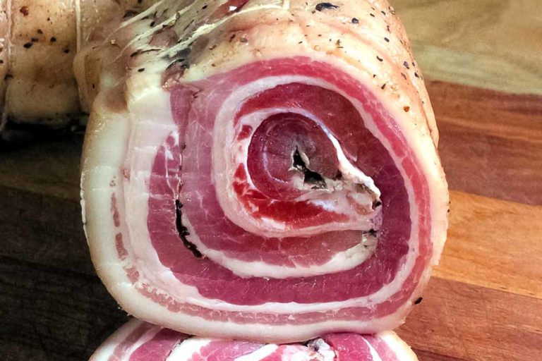 A piece of homemade pancetta sliced to show the circular pattern.
