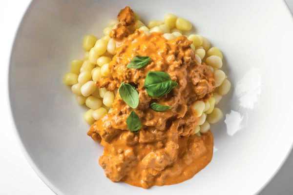 A white bowl filled with leftover meatloaf gnocchi in a creamy tomato sauce that's garnished with fresh basil.