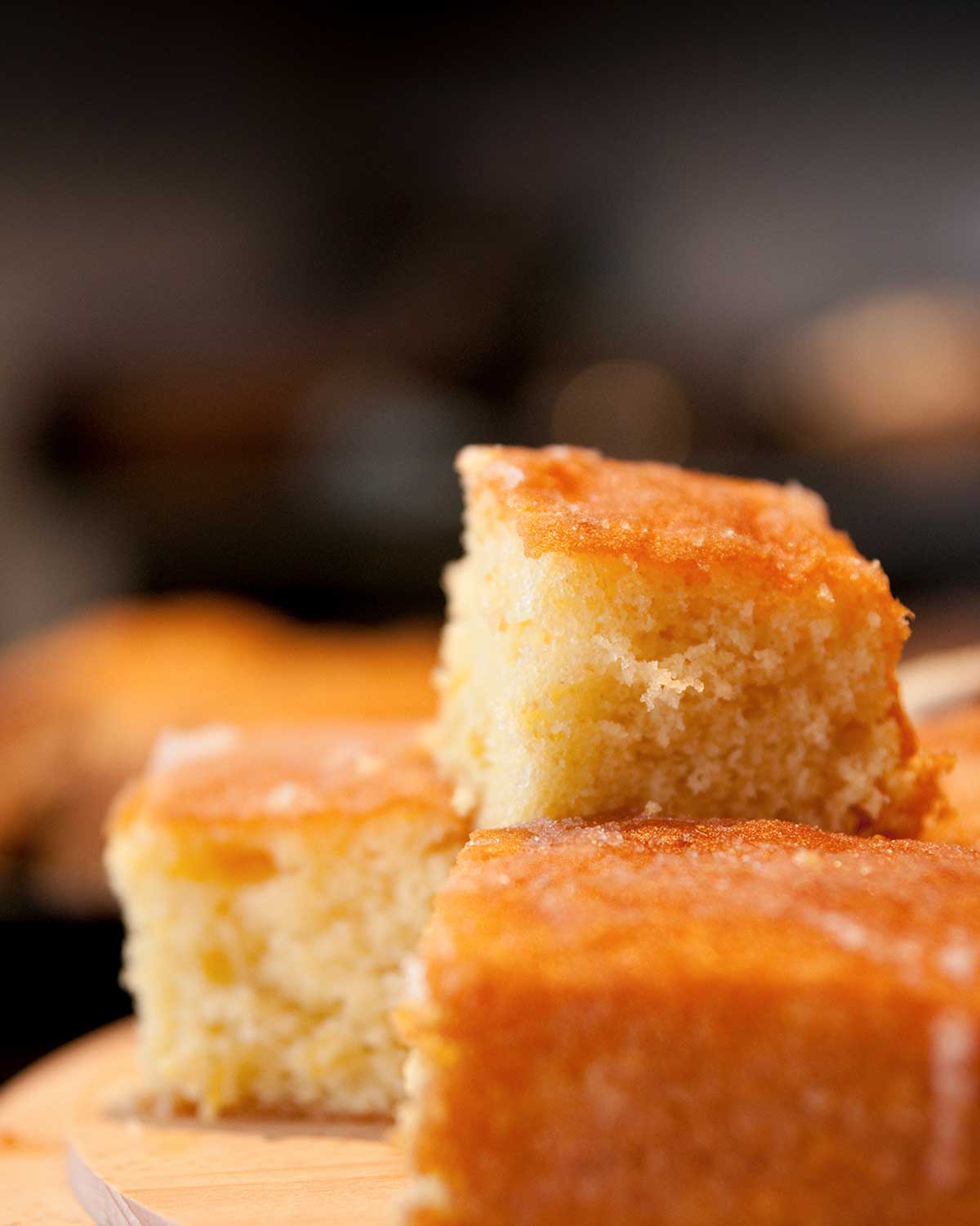 Squares of lemon drizzle cake stacked on top of each other on a wooden board.