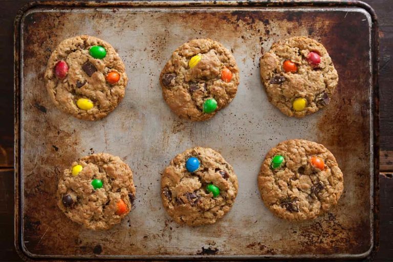 Six peanut butter-oatmeal-chocolate chip cookies on a rimmed baking sheet.