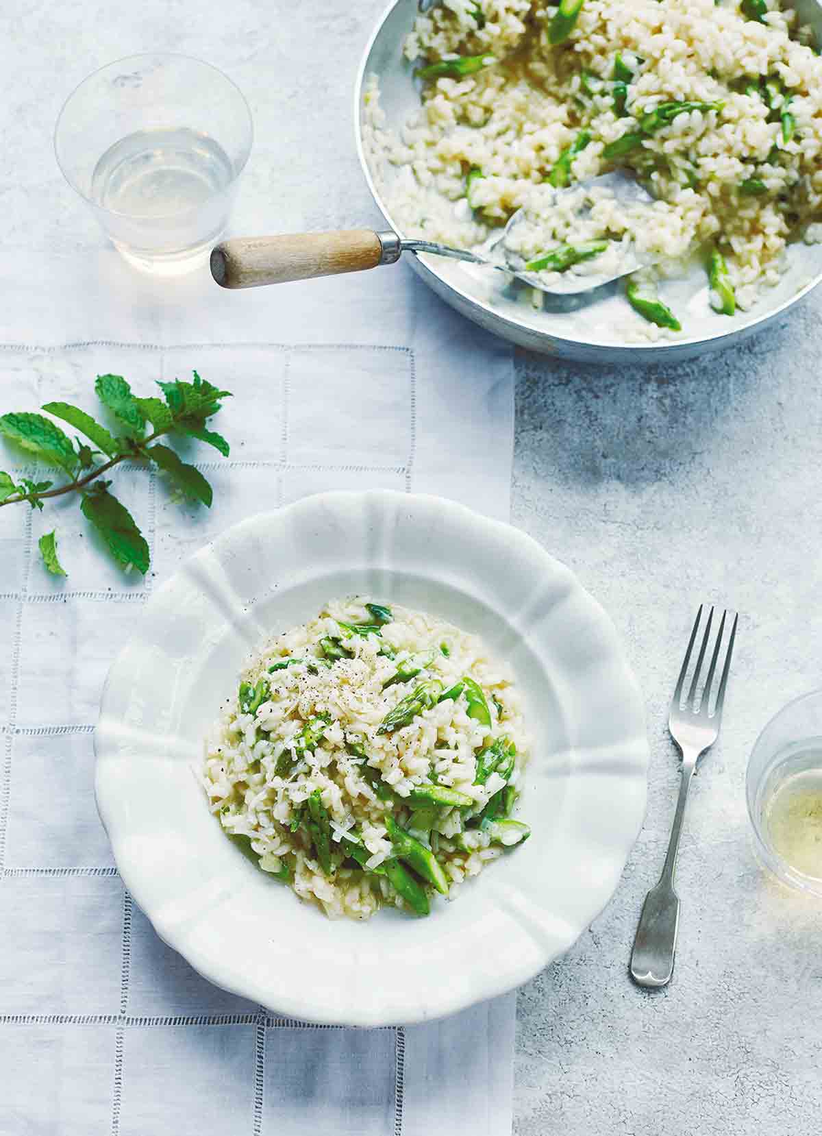 A plate and a bowl of asparagus risotto with a fork resting beside the bowl.