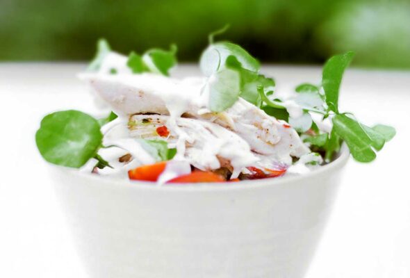 A small white bowl filled with chicken-pea shoot salad.