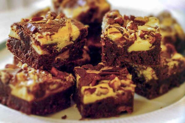 Plate of cream cheese swirl brownies with layers of chocolate, cheese cake, Heath bar, and pecans