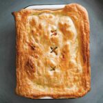 A rectangular dish filled with curry chicken pot pie and topped with puff pastry.