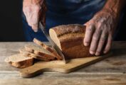 A person slicing a loaf of milk rye bread on a wooden cutting board.