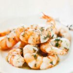 Several pan-fried shrimp with dill piled in a white bowl, garnished with fresh dill.