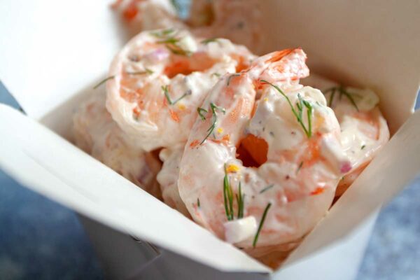 Shrimp salad garnished with dill in a cardboard takeout container.