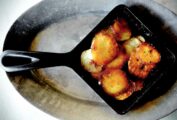 A square cast iron skillet filled with sliced fried skillet potatoes for 2 on a grey oval metal platter.