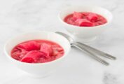 Two white bowls filled with strawberry rhubarb compote and two spoons resting between them.