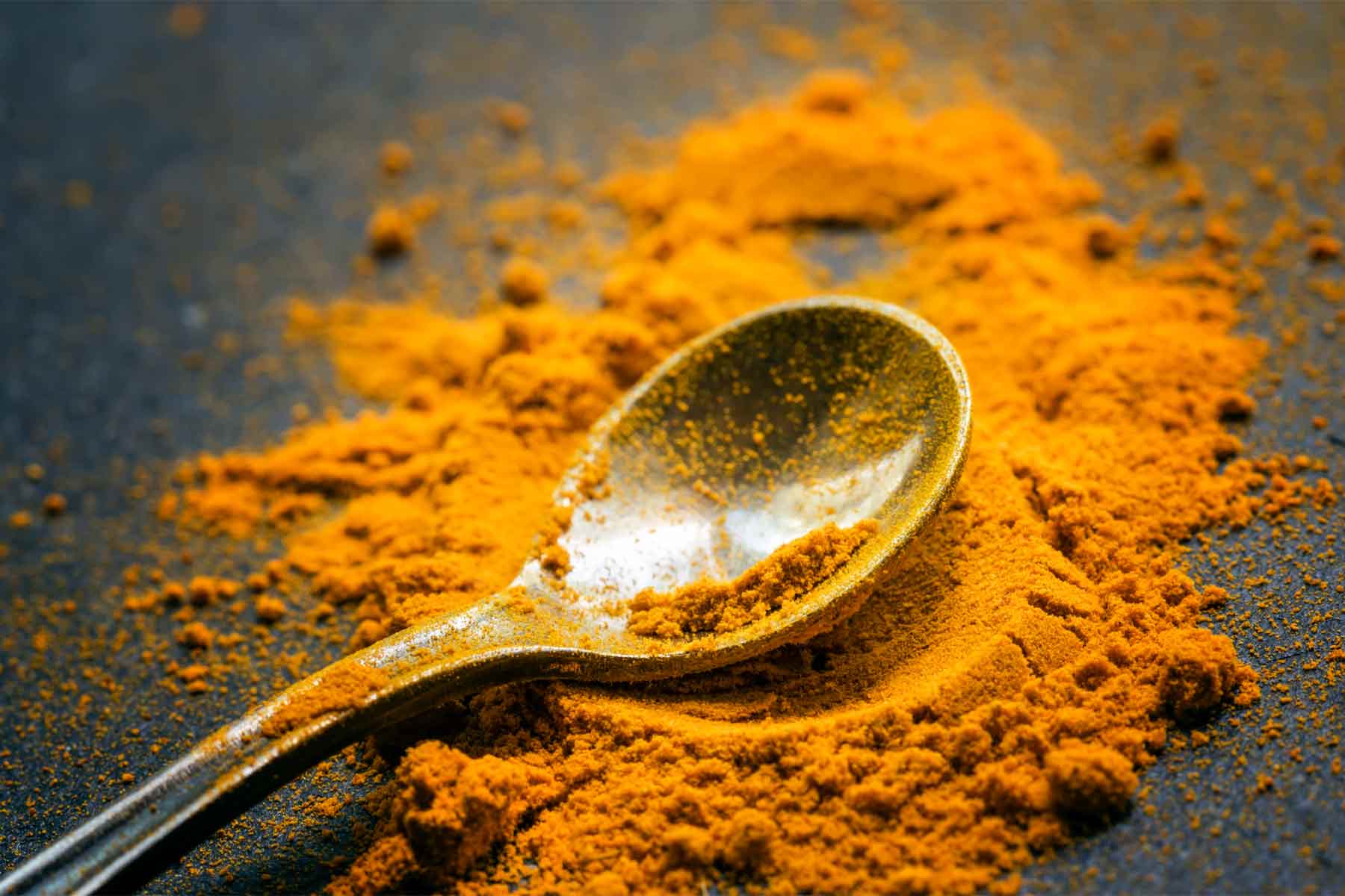 A spoon laying in a pile of turmeric.