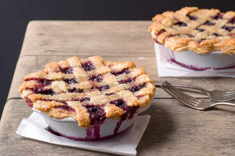 Two individual blueberry pies on on a wooden table with forks beside them.