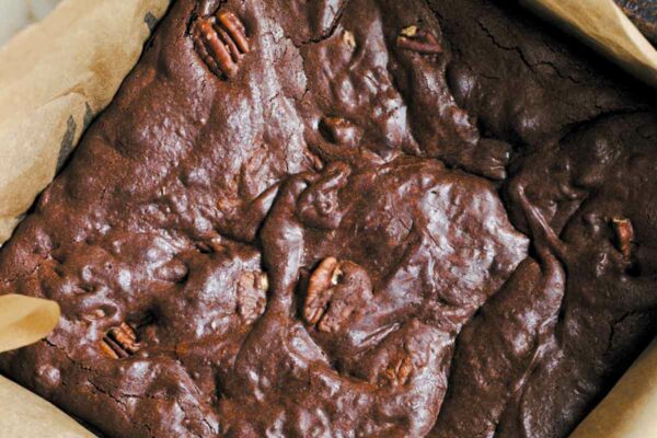 A parchment-lined square pan filled with pecan-studded best brownies.