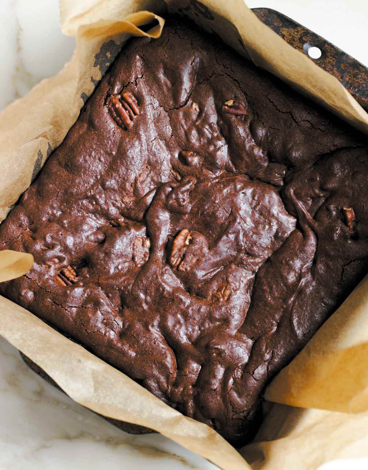 A parchment-lined square pan filled with pecan-studded best brownies.