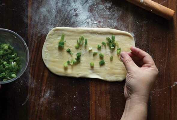 Scallions being scattered over the dough for flaky ribbon pancakes.