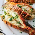 Three grilled lobster tails on an oval platter, garnished with chopped parsley.