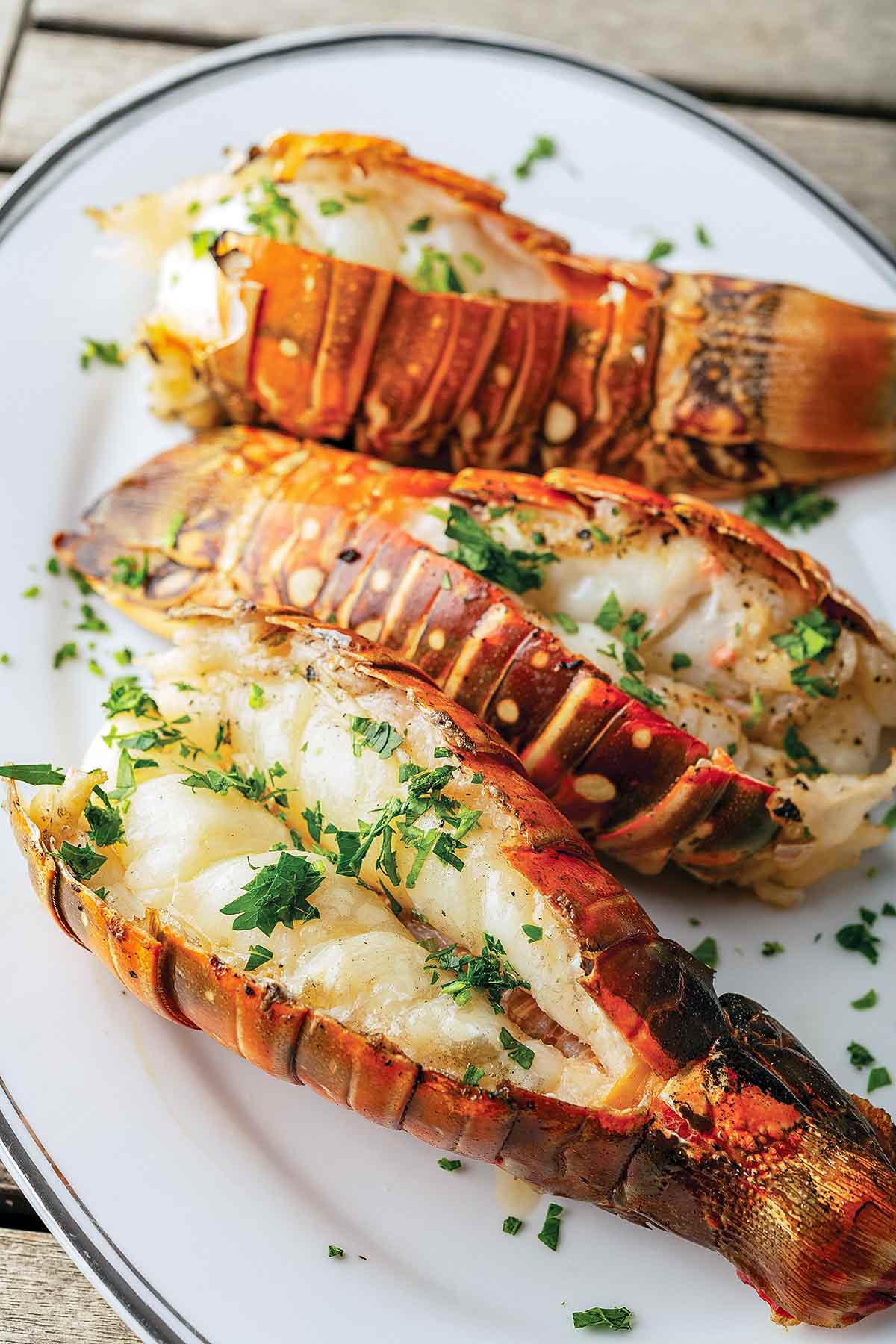 Three grilled lobster tails on an oval platter, garnished with chopped parsley.
