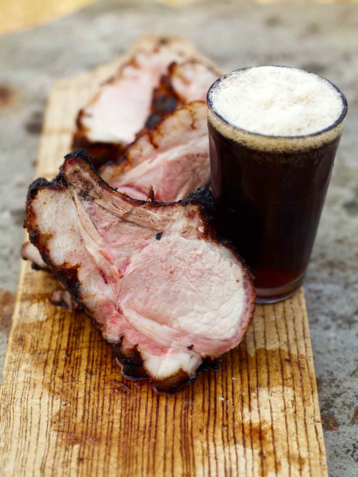 Chops from a spice-glazed grilled pork loin on a cutting board with a glass of stout.