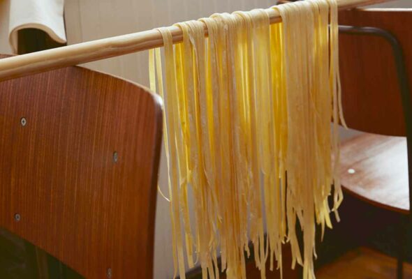 Homemade tagliatelle hanging over a broomstick resting on the back of two chairs.