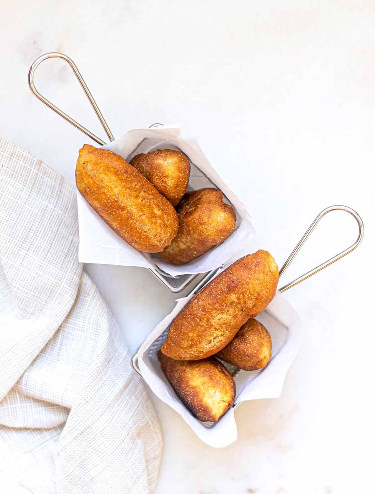 Two metal baskets lined with paper, each with three Jamaican fried dough fritters, or festival.