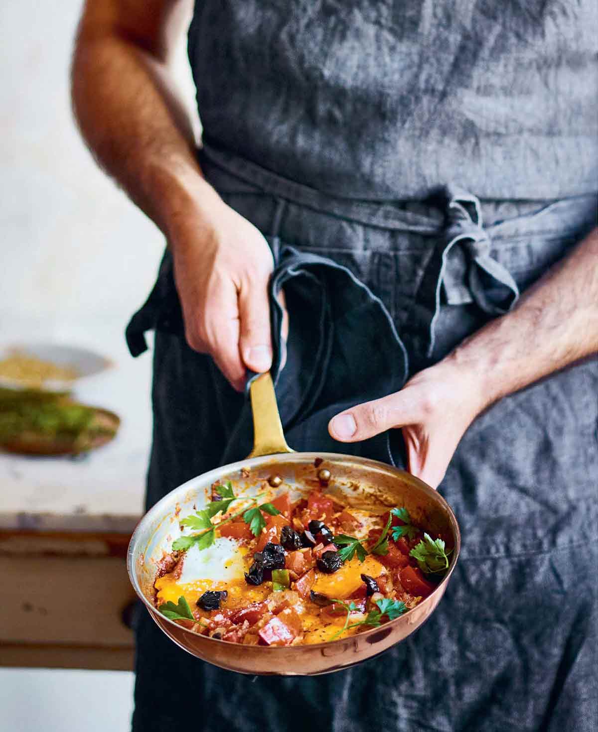 A person holding a skillet with jazmaz, or Syrian shakshuka - eggs cooked in a tomato and chile sauce.