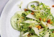 A tangle of raw asparagus salad, pine nuts, and frisee on top of a green dressing.