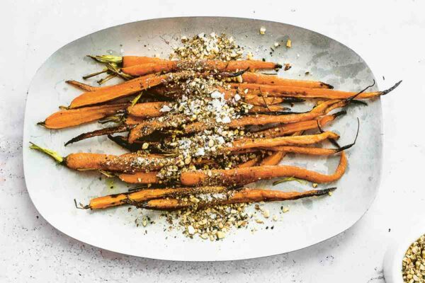 A white oval platter topped with roasted carrots with dukkah and nuts sprinkled on top.