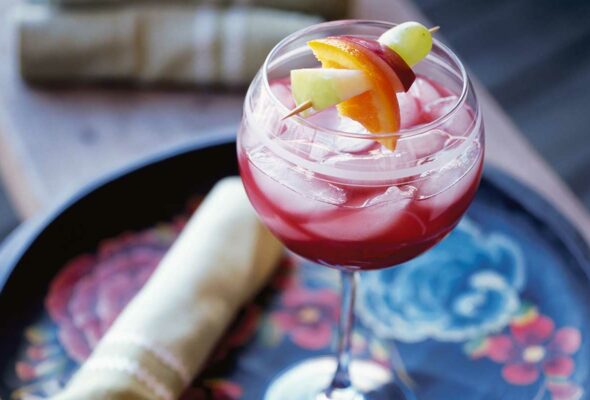 A glass of ruby sangria with a skewer of fruit suspended over the glass on a floral serving tray.