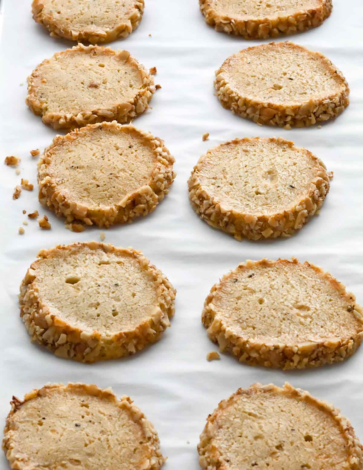 Ten Stilton and walnut crackers arranged in rows on a sheet of parchment.