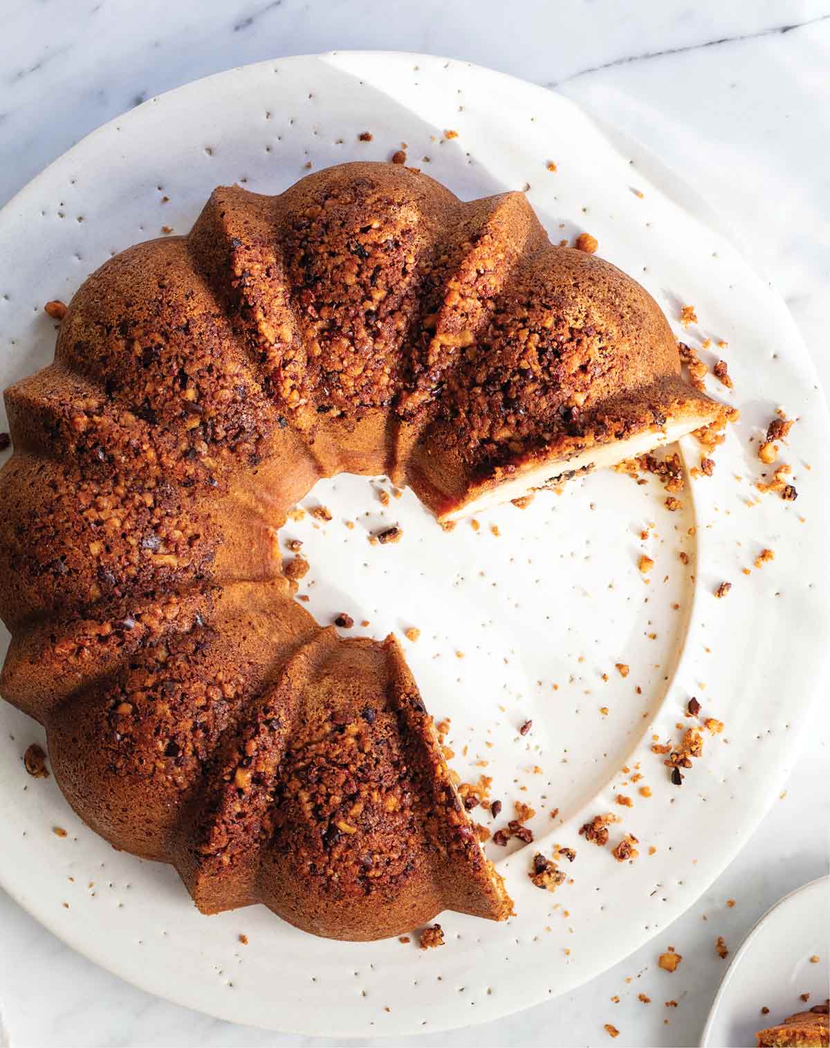 A Bundt-shaped walnut coffee cake with cacao nibs on a white platter with several slices missing.