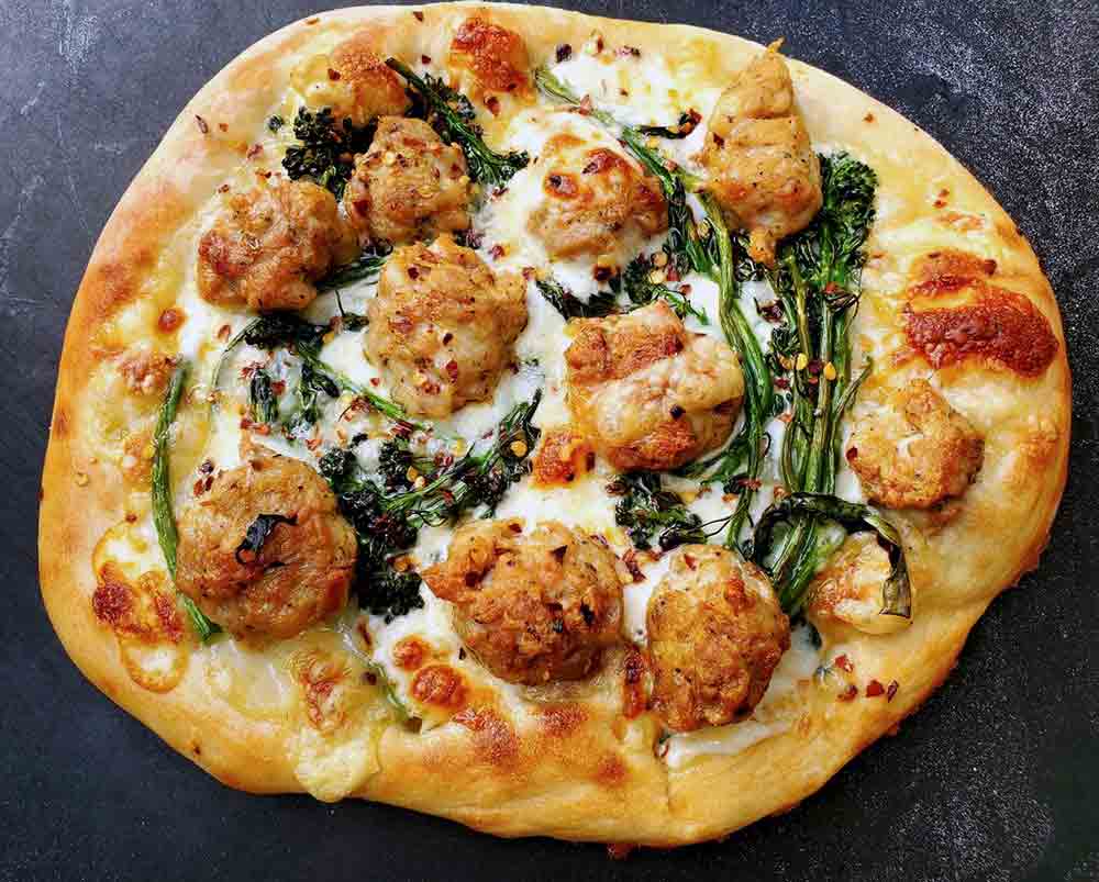 An individual sized white pizza with broccolini, fontina, and sausage.