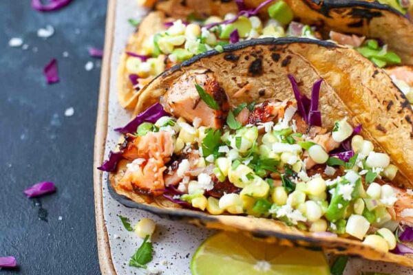 Three wild salmon tacos on a plate with lime halves.