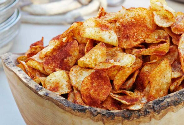 A carved wooden bowl filled with barbecue potato chips.
