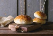 Three burger buns topped with sesame seeds on a wooden surface.