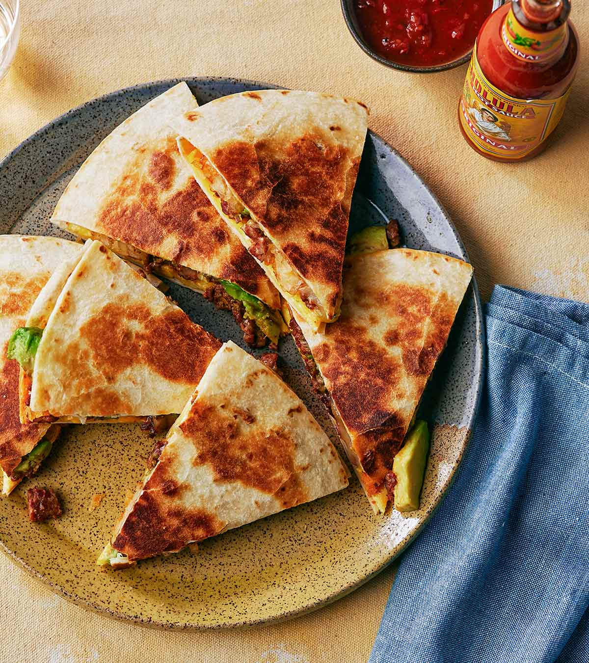 A California breakfast quesadilla, cut into eight wedges on a plate with a bottle of hot sauce on the side.